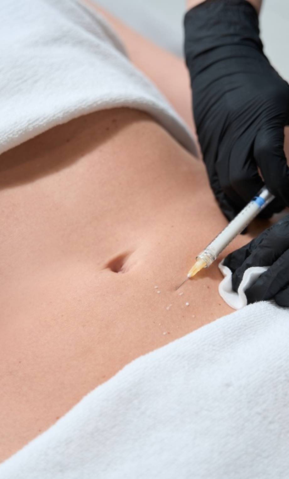 Female in black gloves makes injections in the belly of a client, a woman lies on a cosmetology couch